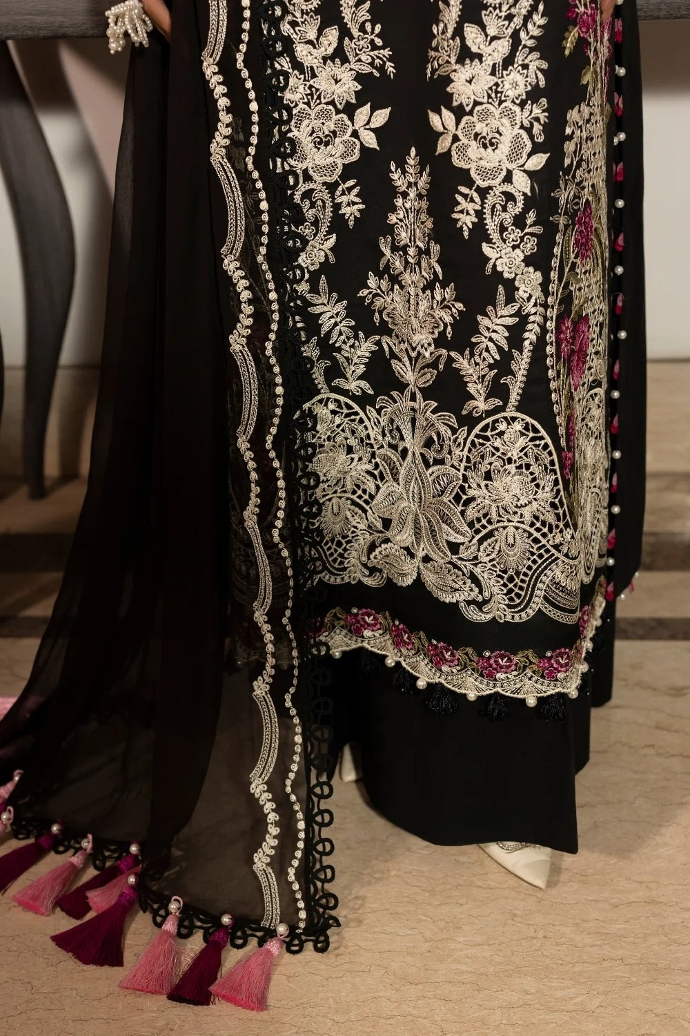 Black traditional outfit with intricate white embroidery on a wooden floor.