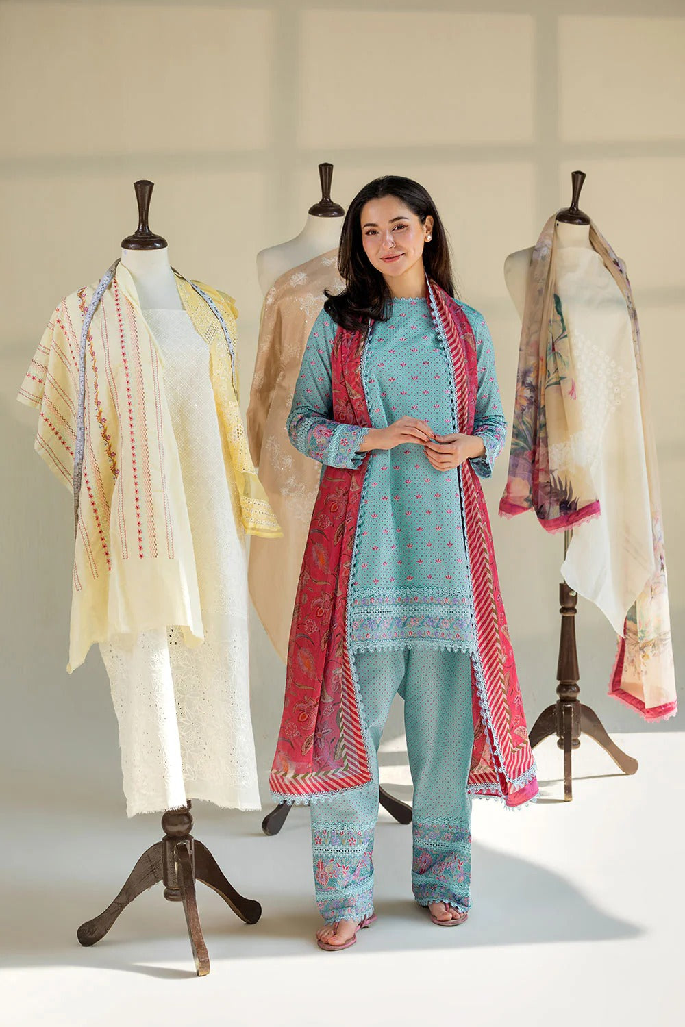 Woman in traditional outfit with embroidered shawl and pants, standing in front of mannequins with similar attire.