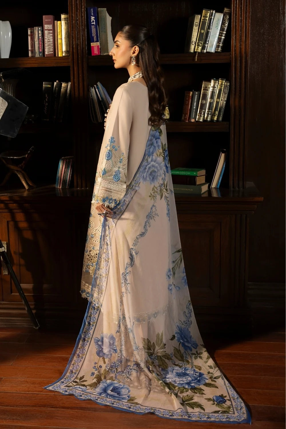 Woman in a white and blue floral saree standing in front of a bookshelf.
