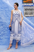 Woman in a white and blue embroidered dress standing against a blue wall.