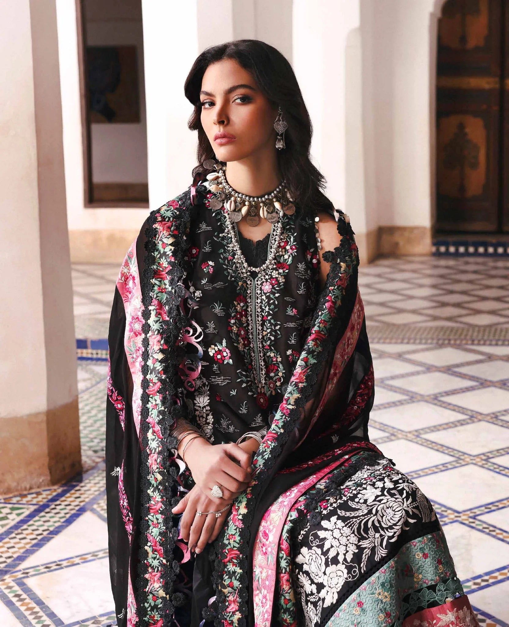 Woman wearing a black embroidered outfit with floral patterns in an ornate interior setting