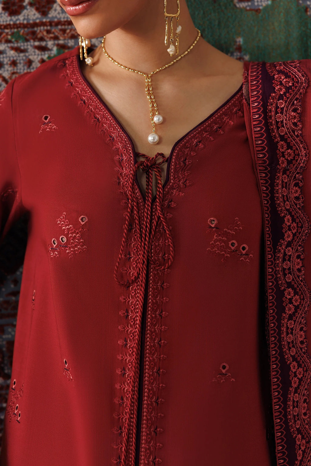 A close-up of a woman wearing a deep red embroidered traditional outfit with a V-neckline, tie-front detail, and matching embroidered dupatta. Gold jewelry is also visible.