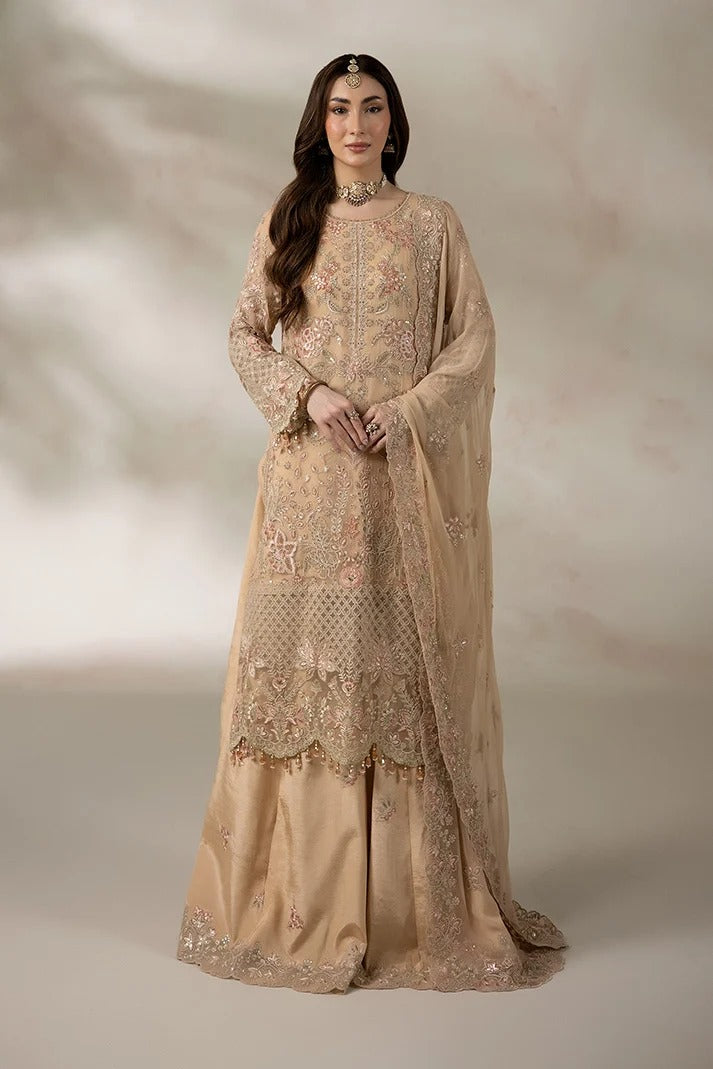 A woman models a traditional beige embroidered Anarkali suit with a matching sheer dupatta, set against a soft, textured beige studio backdrop.