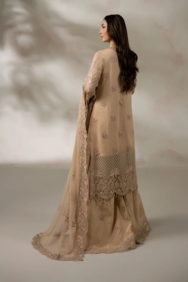 A woman modeling a beige traditional outfit with intricate embroidery and a matching dupatta, shown from the back against a soft neutral studio backdrop.