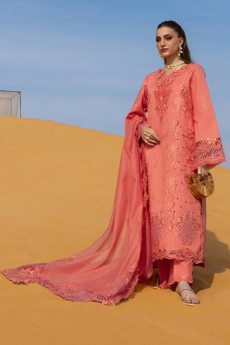 Woman in a pink embroidered outfit standing in desert sand with blue sky.