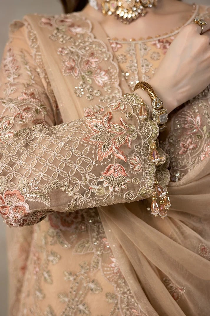 Close-up of a person wearing an ornate beige traditional outfit with intricate floral embroidery, lace sleeves, and a matching draped scarf, accessorized with a statement necklace and bracelet.