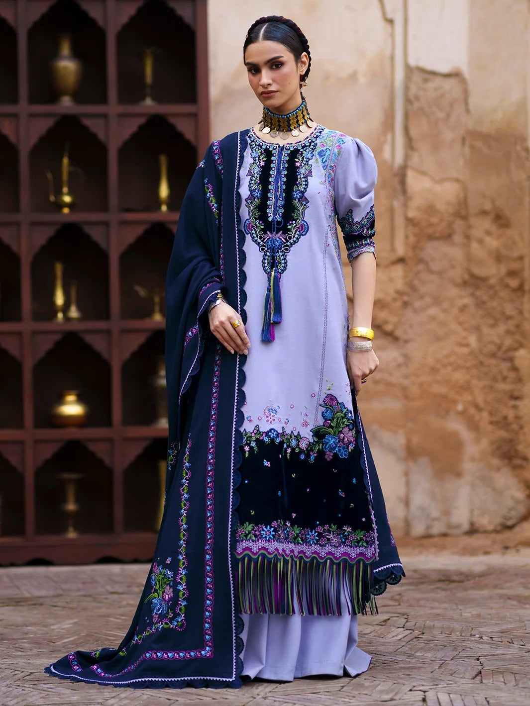 A woman models a traditional South Asian salwar kameez suit. The outfit features a lavender kameez kurta with intricate multicolor floral embroidery and a navy blue border, paired with a matching navy blue dupatta.