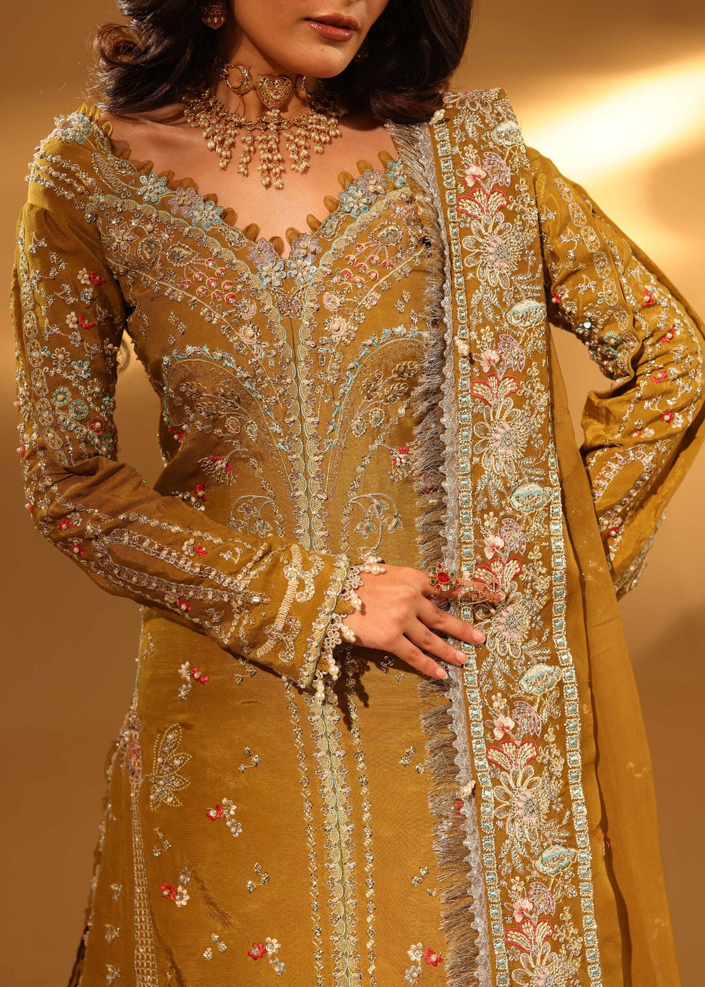 Woman wearing a mustard yellow embroidered traditional outfit with intricate designs.
