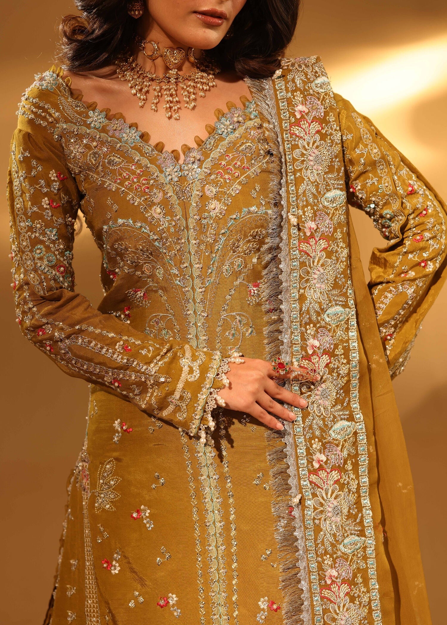 Woman wearing a mustard yellow embroidered traditional outfit with intricate designs.