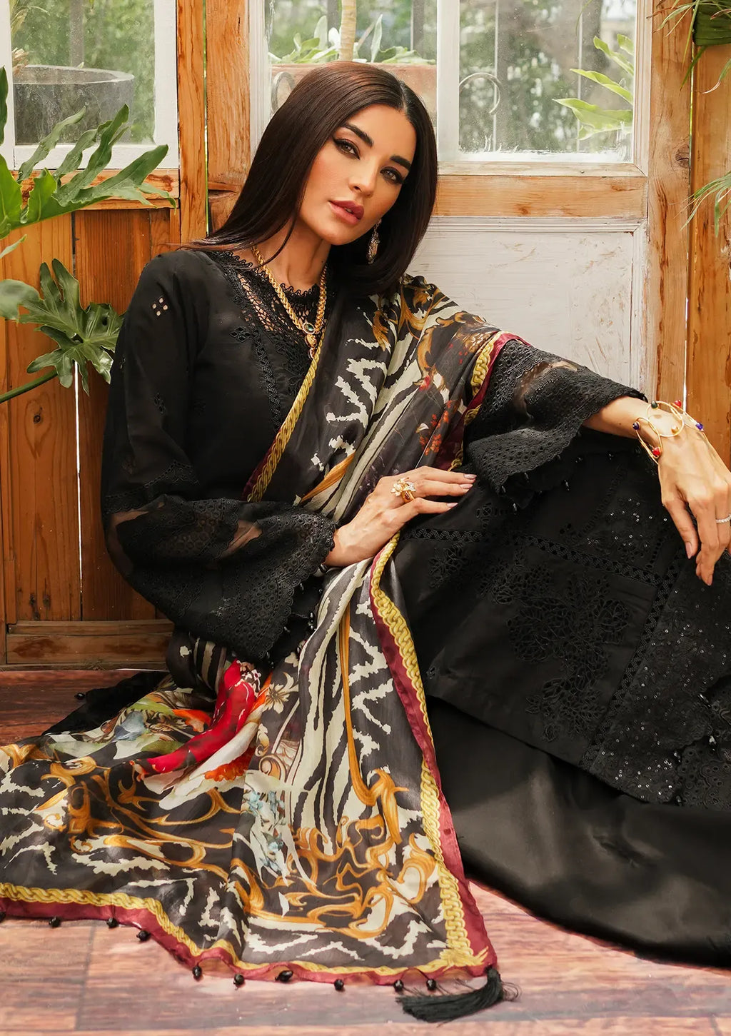 A woman models a black embroidered traditional outfit with a patterned dupatta in front of a rustic wooden door.