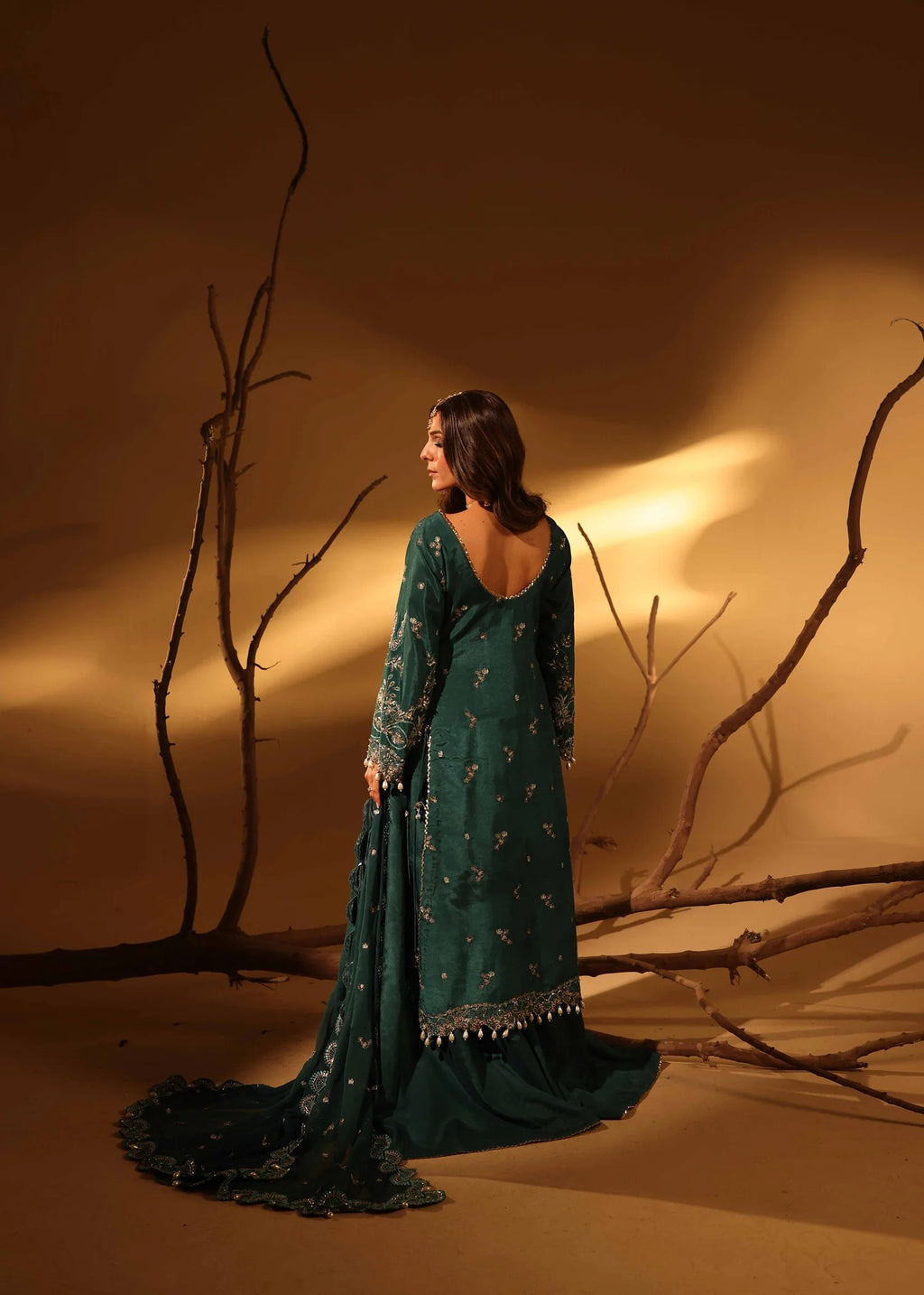 Woman in a green traditional outfit standing in a desert-like setting with dry branches.