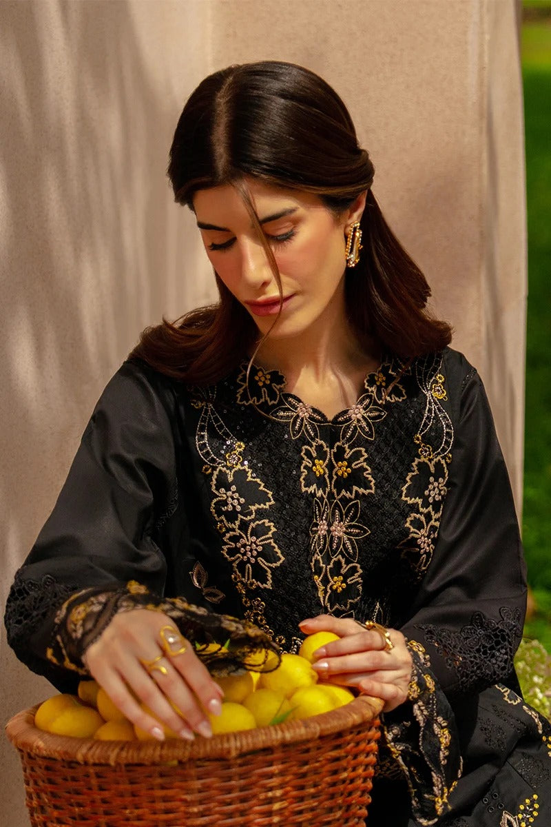 Woman in a black embroidered dress holding lemons in a basket against a neutral background
