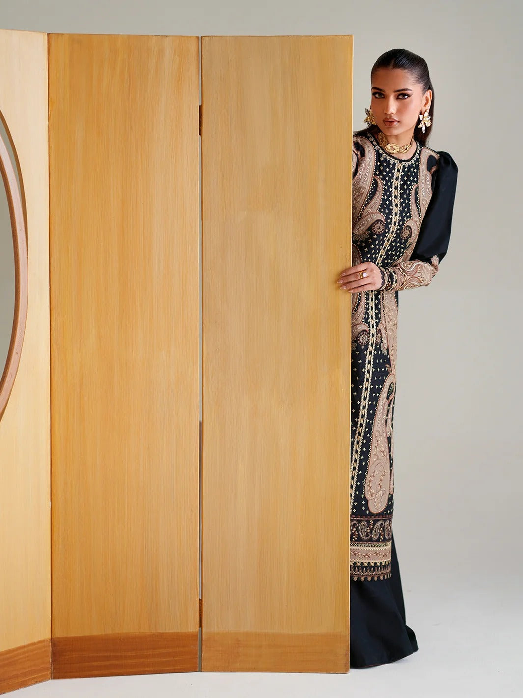Woman in a patterned dress peeking from behind a wooden wardrobe