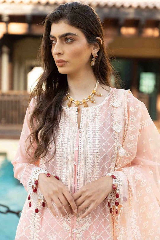 Woman wearing a light pink embroidered outfit with gold jewelry outdoors.