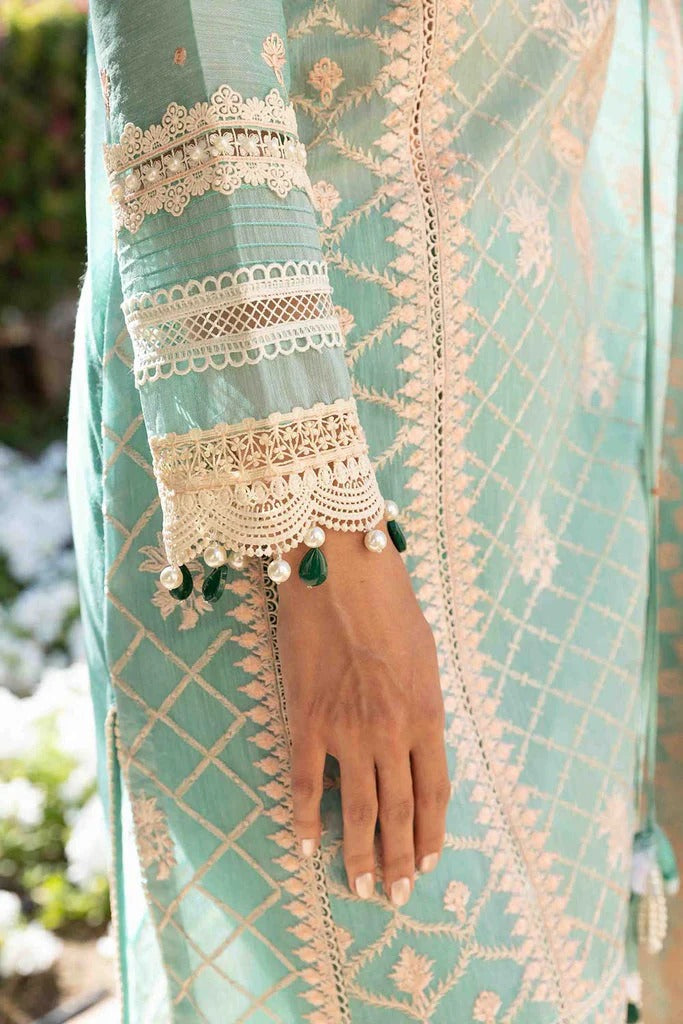 Teal embroidered garment with a hand wearing a bracelet, blurred background