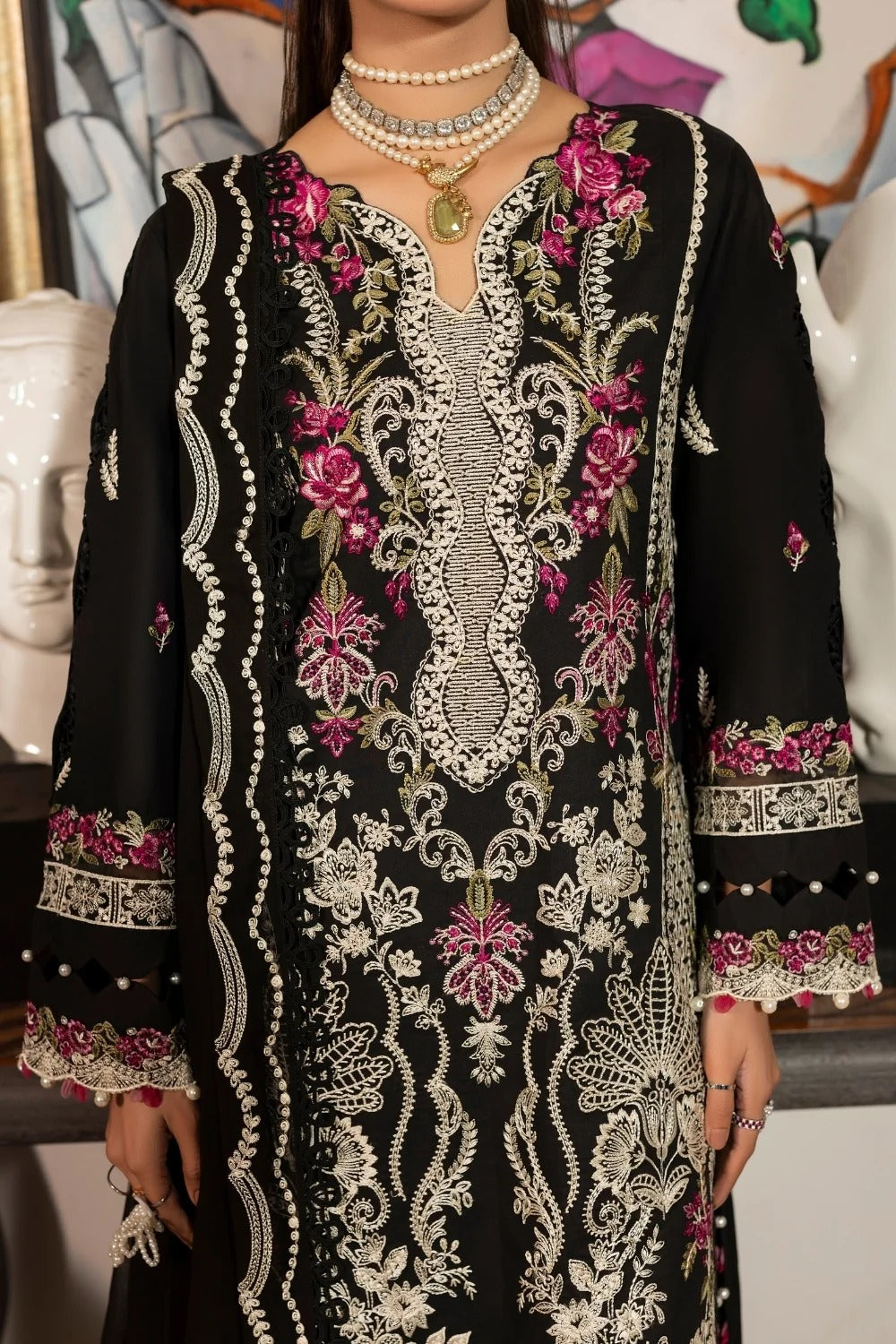A black traditional embroidered tunic with intricate silver and pink floral embroidery, worn by a model with layered pearl necklaces.