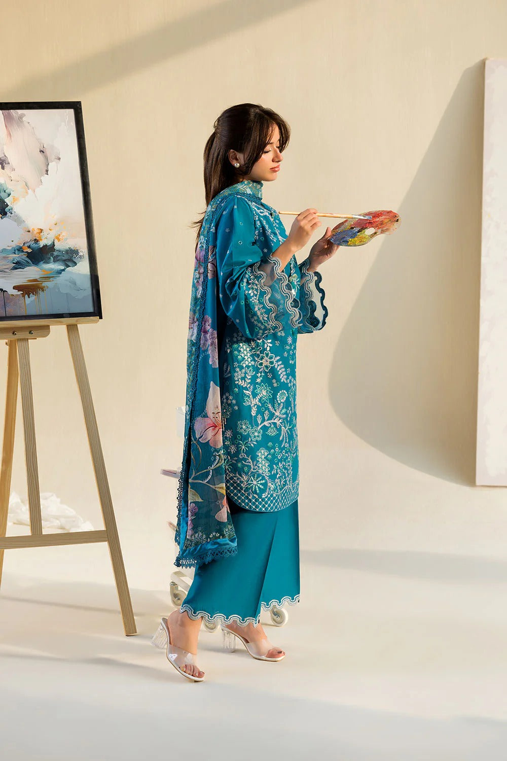 Woman in a blue traditional outfit holding a paintbrush in a minimalistic setting