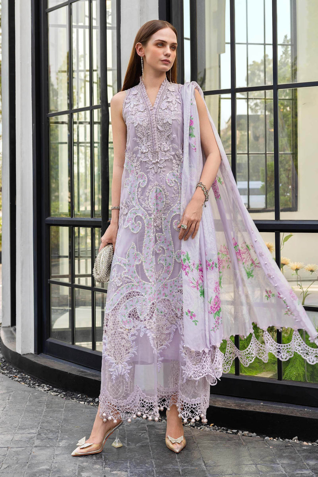 Woman in a light purple embroidered outfit with a floral dupatta standing in front of a glass door.