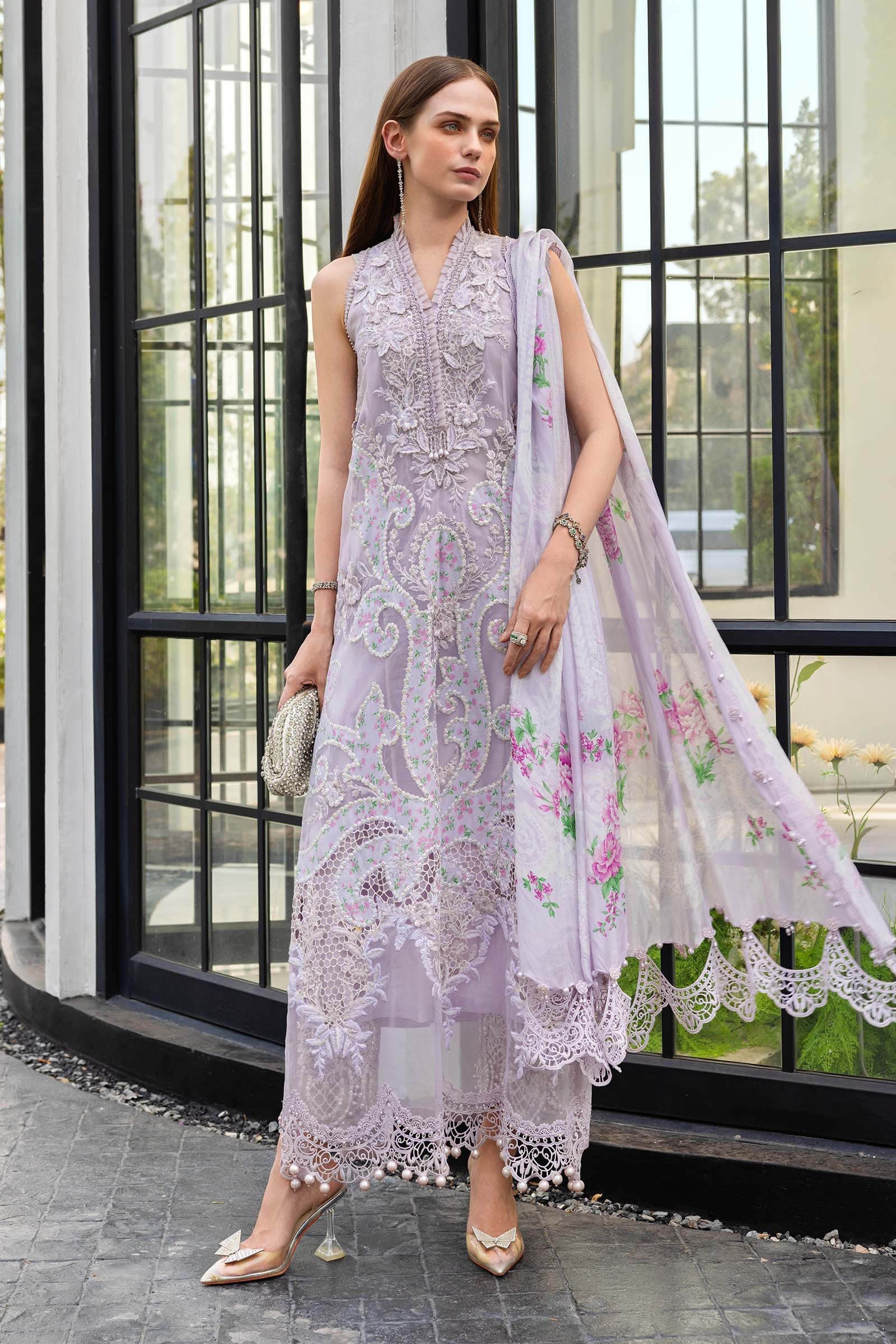 Woman in a light purple embroidered outfit with a floral dupatta standing in front of a glass door.