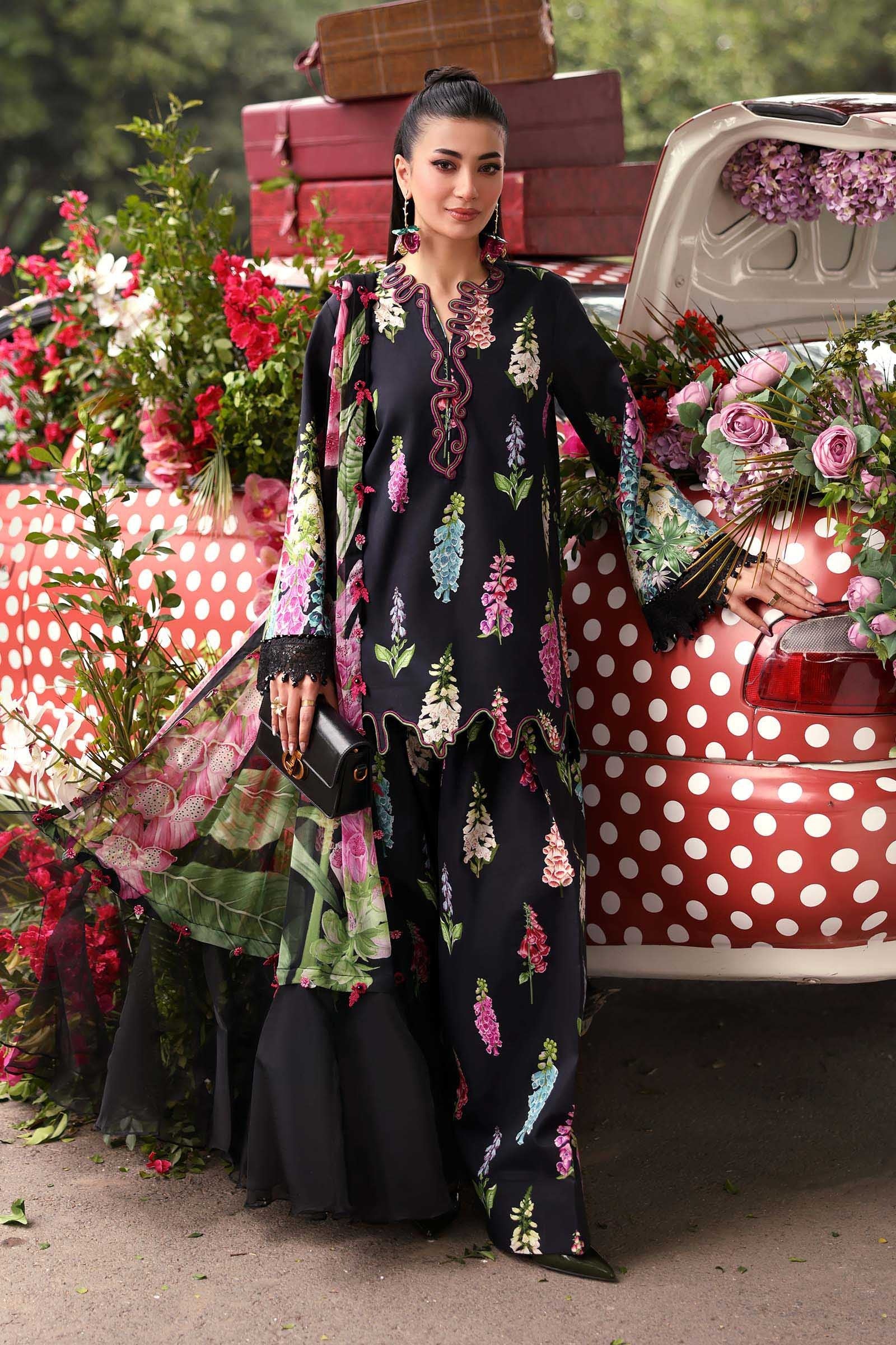 Woman in a floral outfit standing in front of a vintage car with floral decorations.