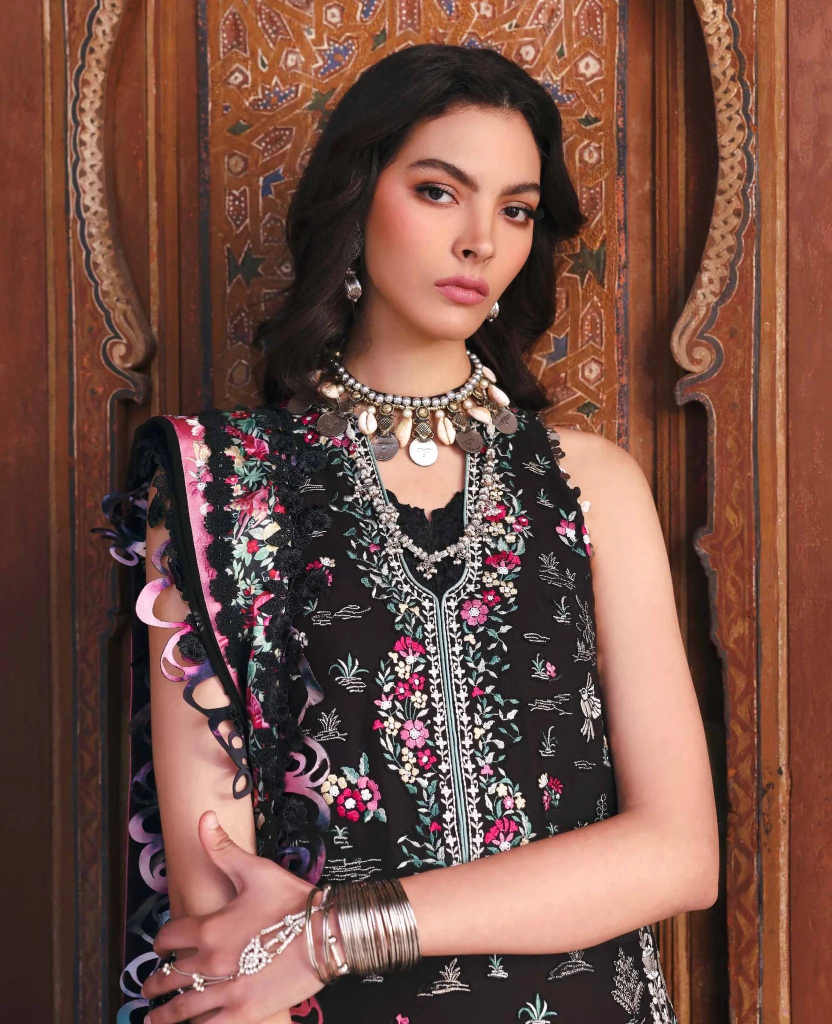 Woman wearing a black floral sleeveless top with intricate designs against a decorative wooden background