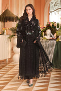 A woman models a long black embroidered abaya with sheer sleeves and tassel fringe, standing in an elegant indoor setting with a checkered floor and floral decor.