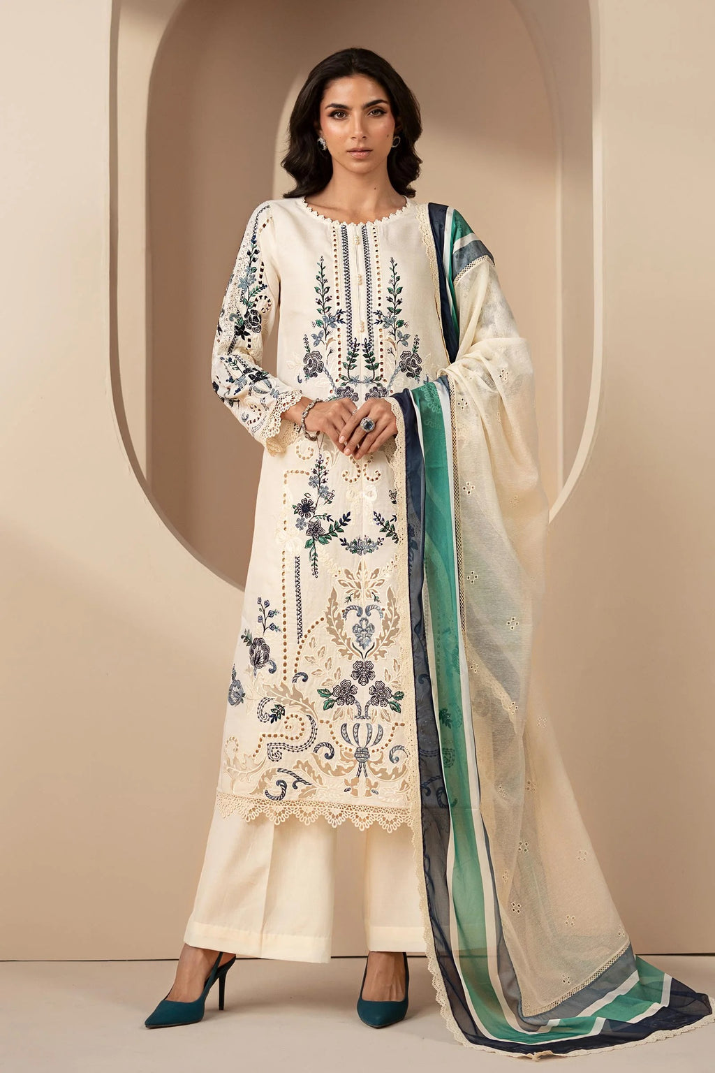 Woman wearing an embroidered white dress with a green dupatta against a beige background