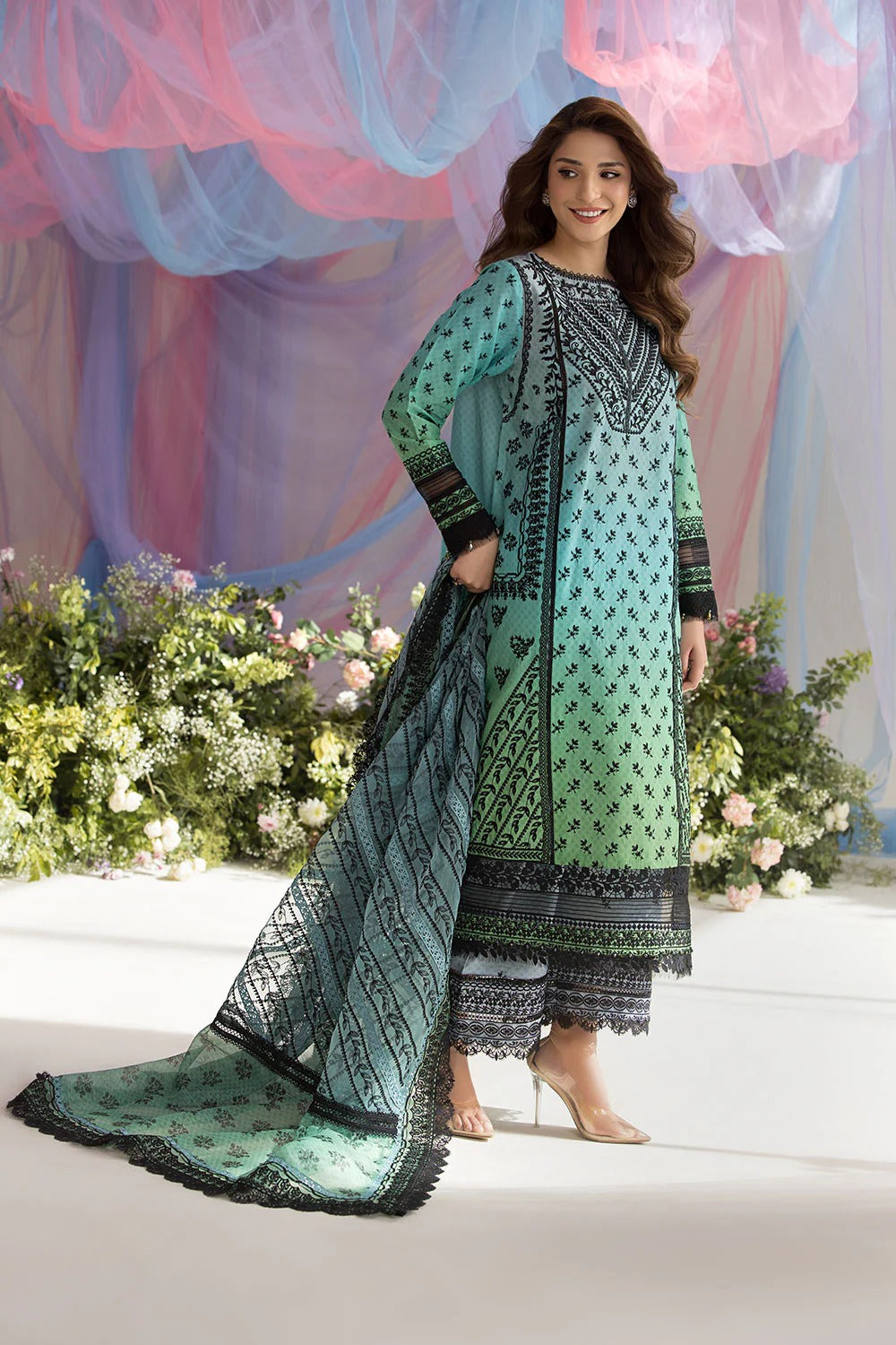 Woman in a green and black patterned outfit standing in front of floral decorations.