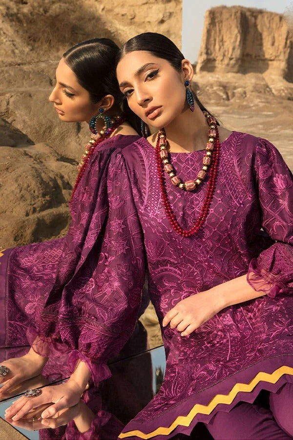 A woman wearing a purple embroidered kurta with matching trousers and red beaded necklaces, posed outdoors against a rocky desert background with a mirrored reflection showing the back of the outfit.