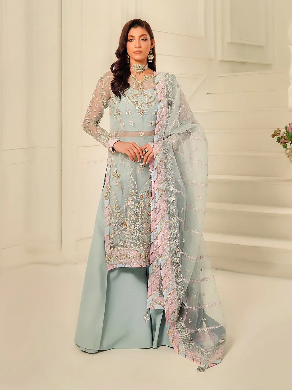 Woman wearing a light blue embroidered traditional outfit with a matching dupatta in a neutral setting.