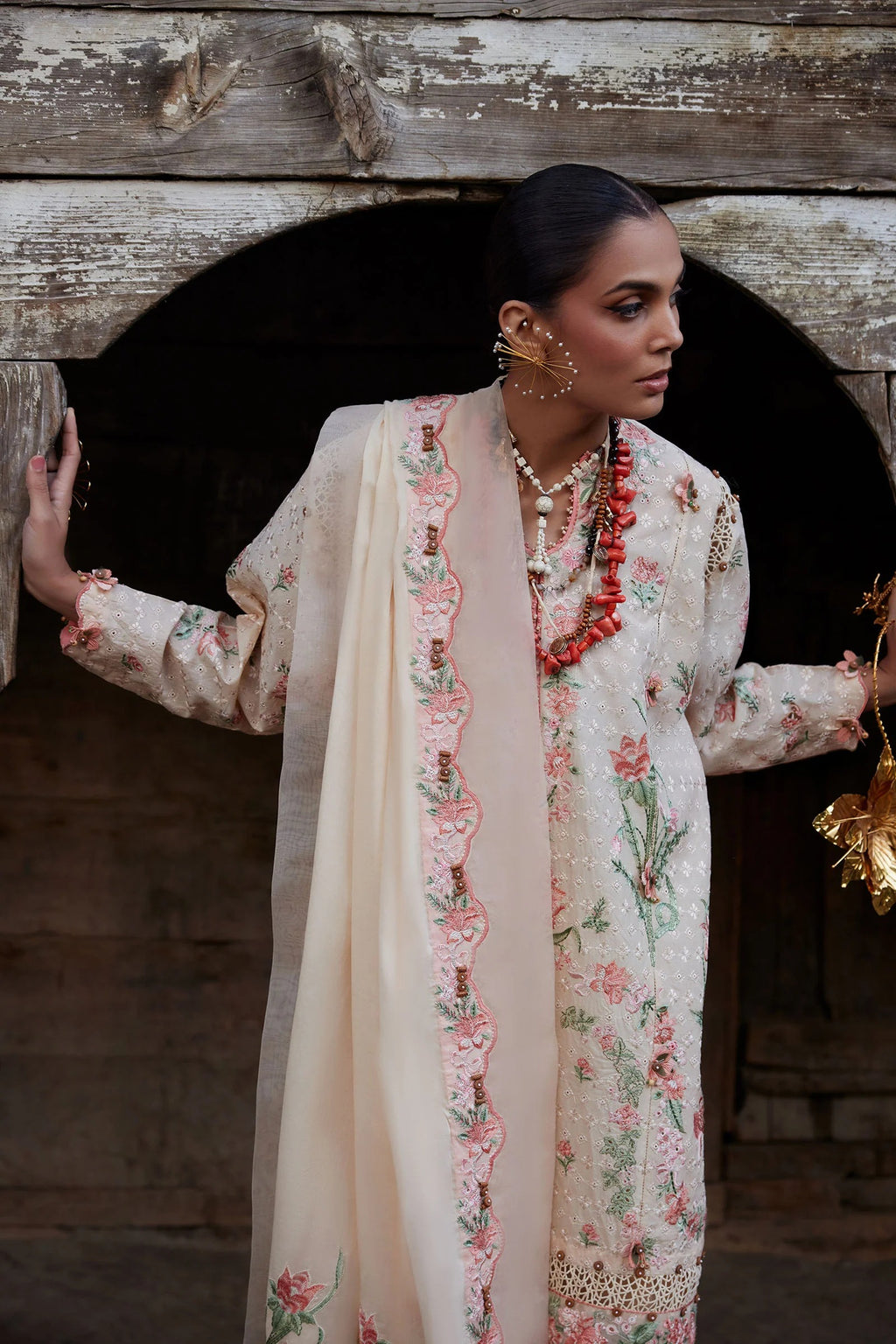 Woman in a floral outfit standing in front of a wooden archway.