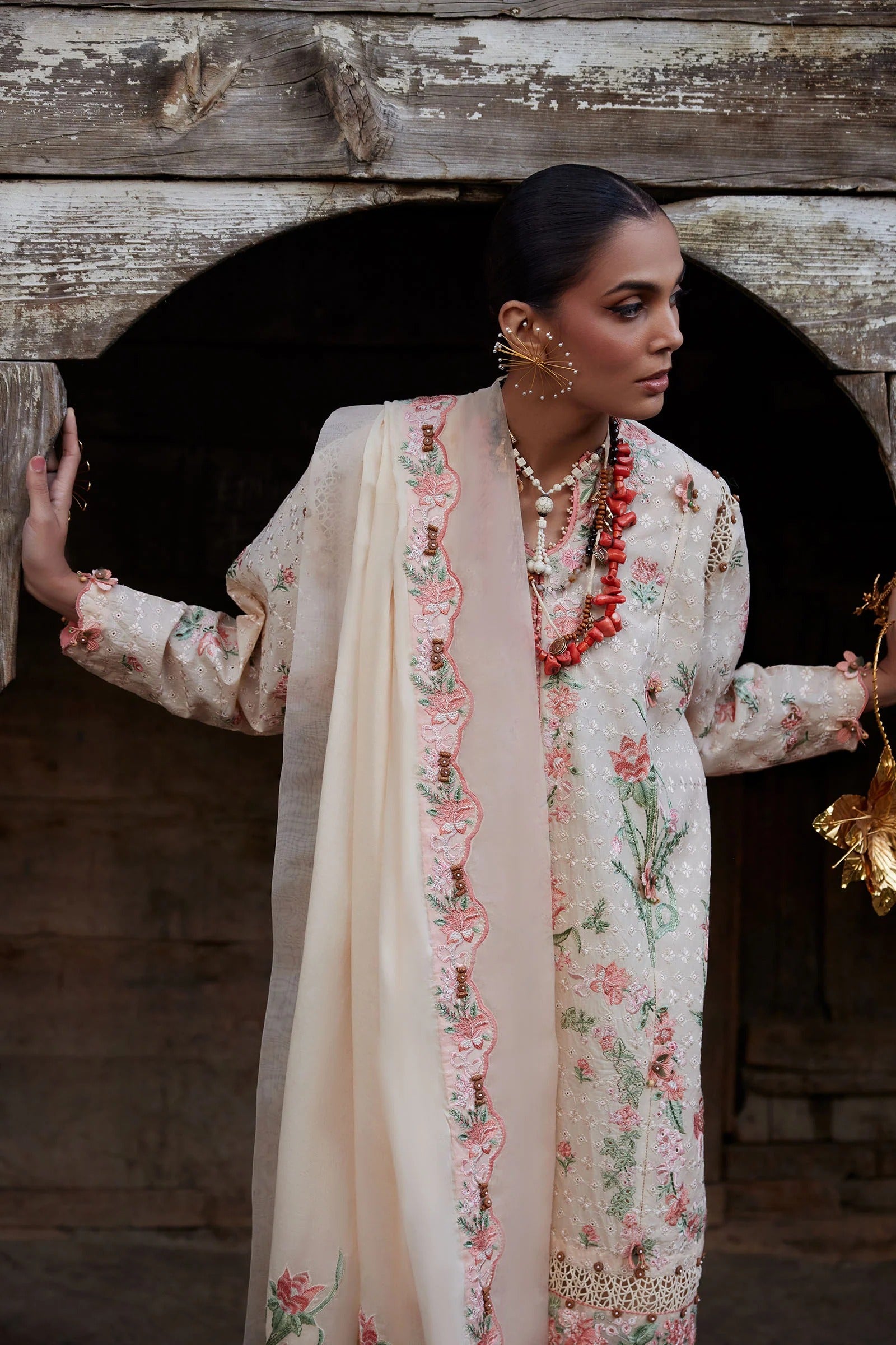 Woman in a floral outfit standing in front of a wooden archway.