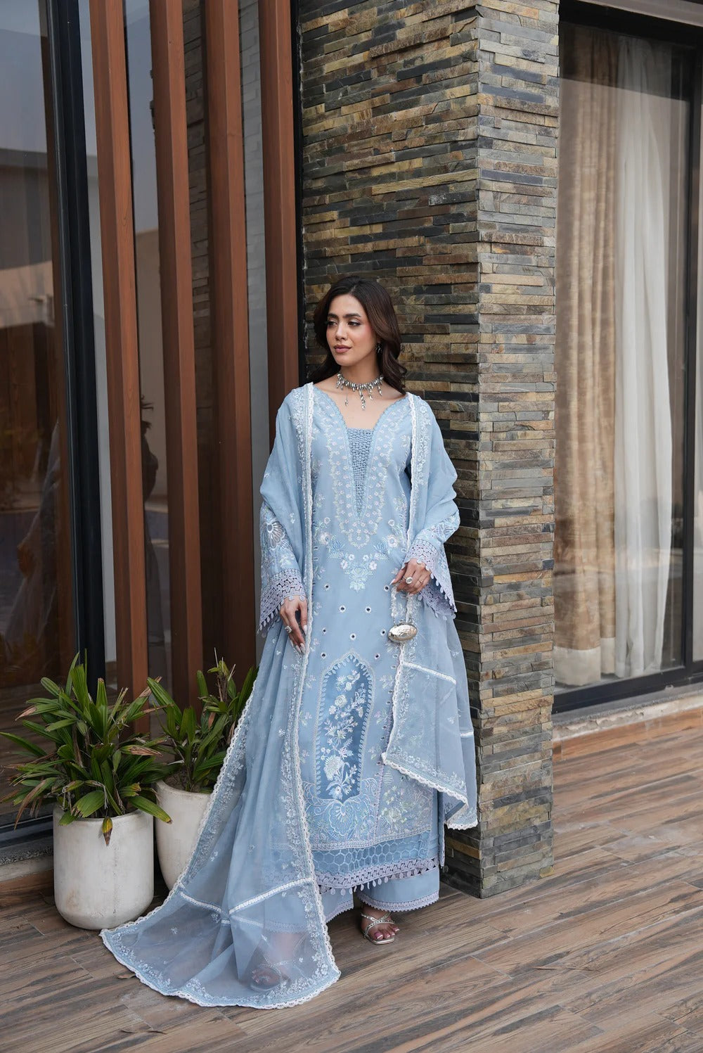 Woman in a light blue embroidered outfit standing in front of a stone wall.