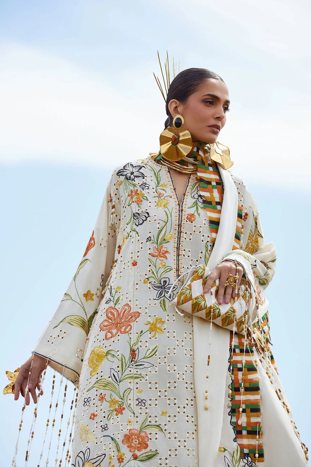 Woman wearing a floral embroidered outfit with a colorful scarf against a clear blue sky.
