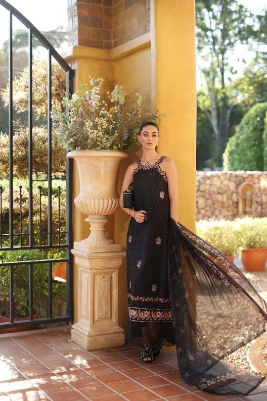 Woman in a black dress with floral embroidery standing next to a decorative column outdoors.