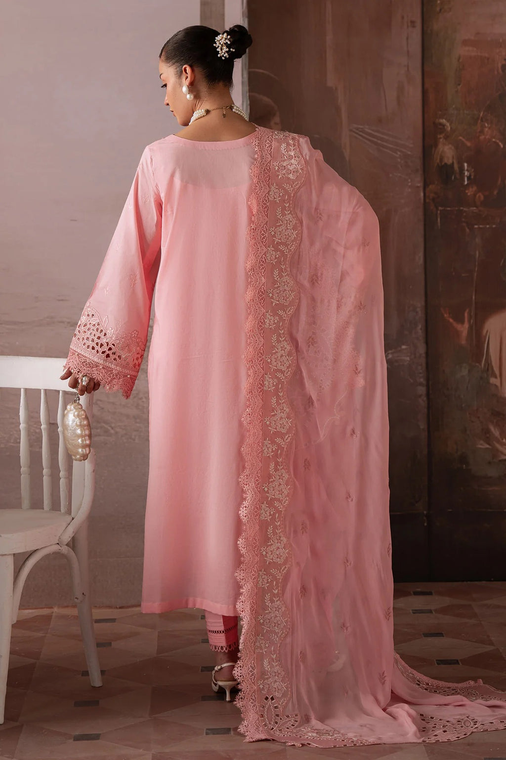 Woman wearing a pink traditional outfit with intricate lace details in a room.