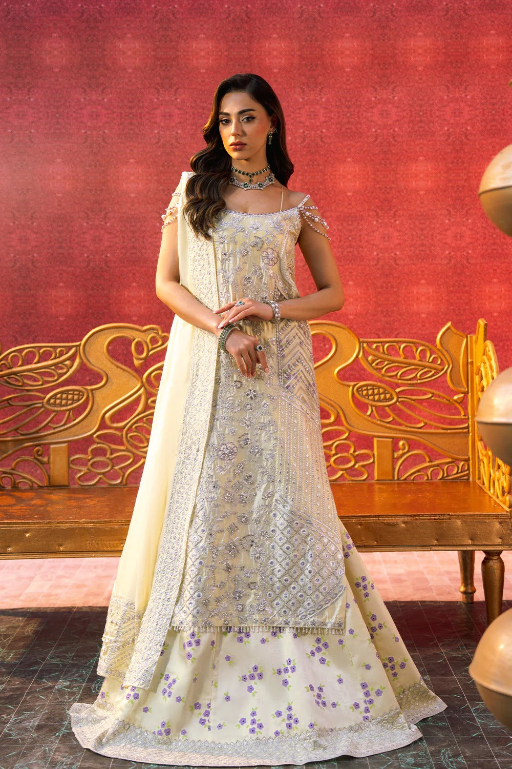 Woman in a traditional embroidered dress standing against a decorative red and gold wall.