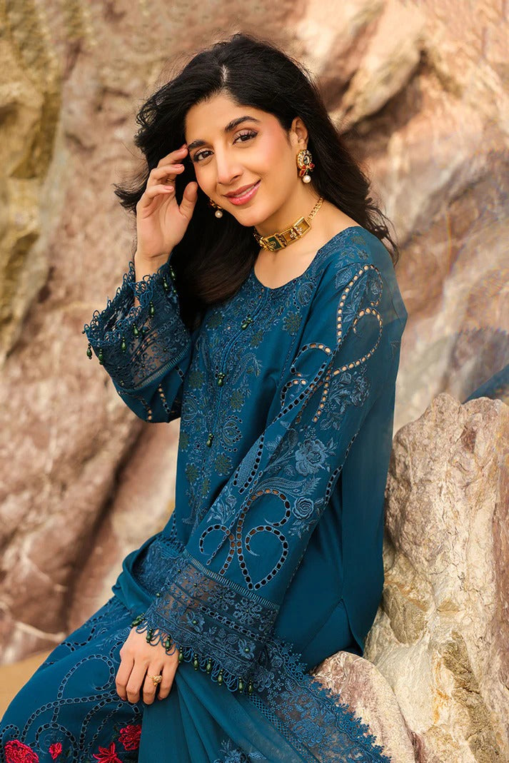 Woman in a blue embroidered outfit sitting against a stone wall