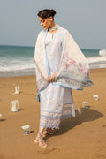 Woman in a floral dress and shawl standing on a beach with ocean in the background