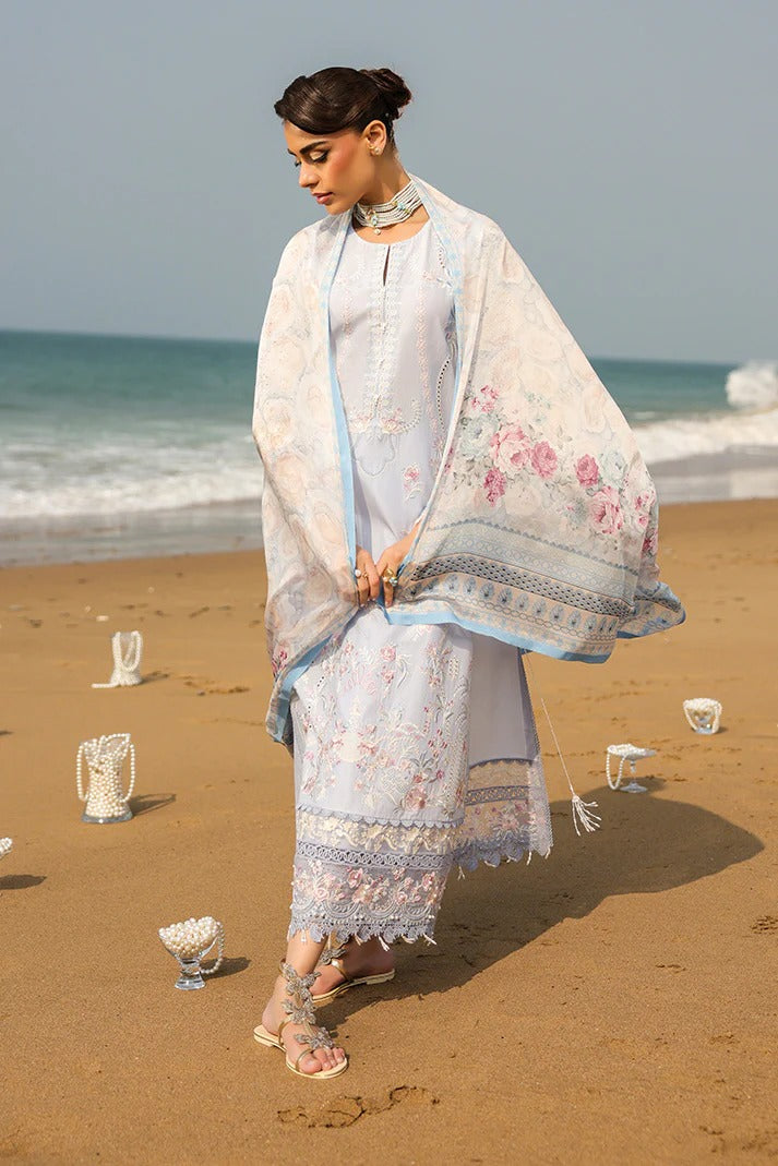 Woman in a floral dress and shawl standing on a beach with ocean in the background