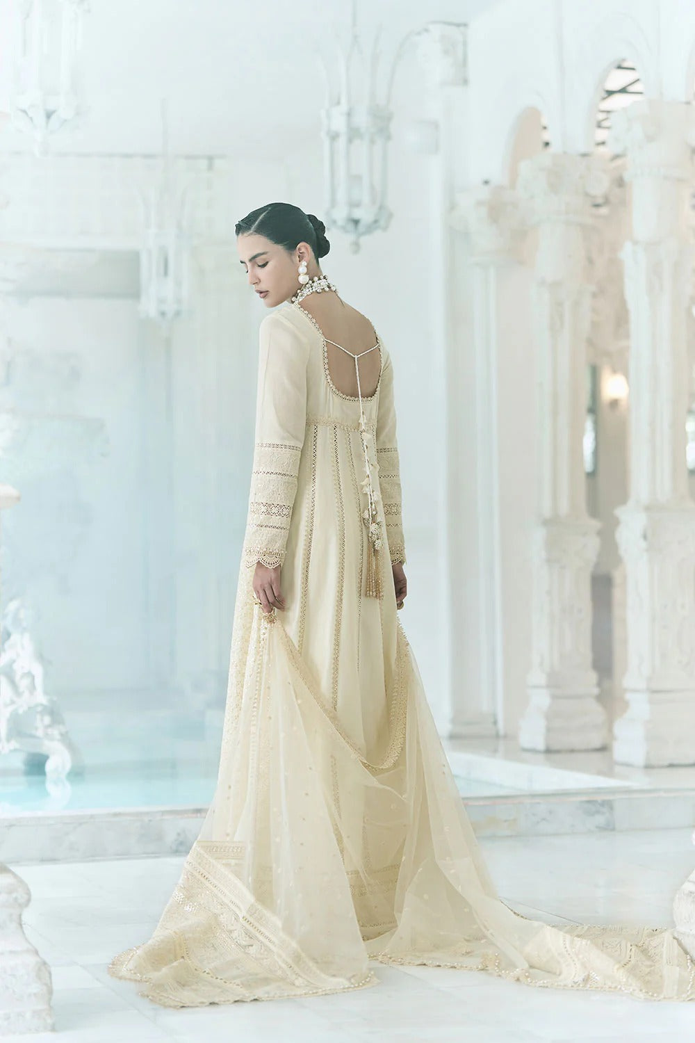 Woman in a long, light-colored dress standing in a white, elegant interior setting.