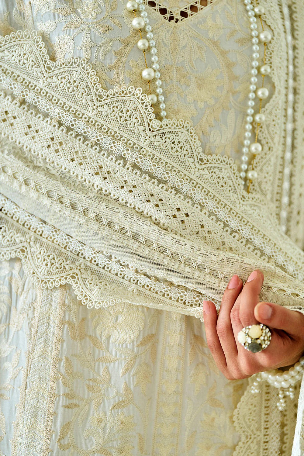 Close-up of a hand holding a lace fabric with intricate patterns and pearl-like beads.
