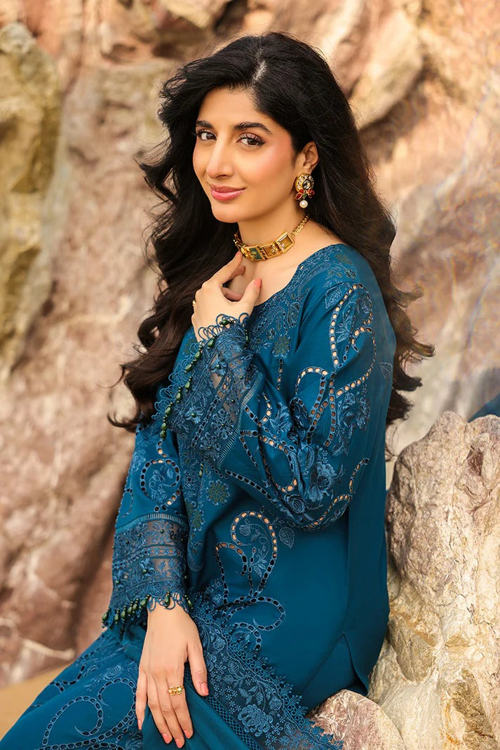 Woman in a blue embroidered outfit sitting against a stone wall.