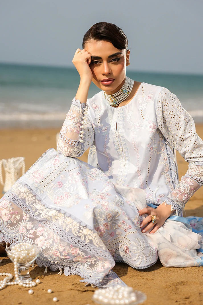 Woman in a white embroidered outfit sitting on a beach with ocean in the background