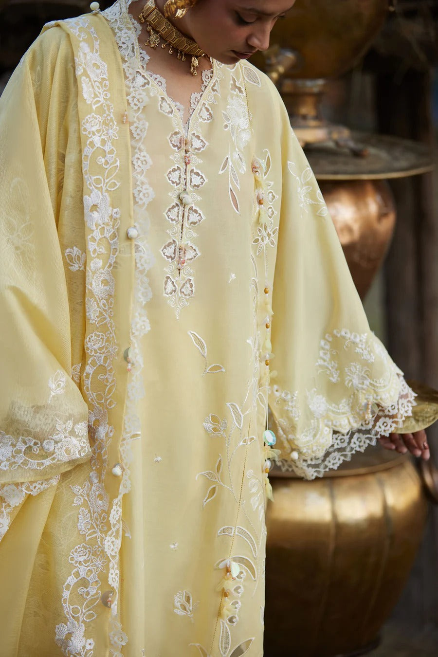 Woman wearing a light yellow embroidered dress with intricate patterns.