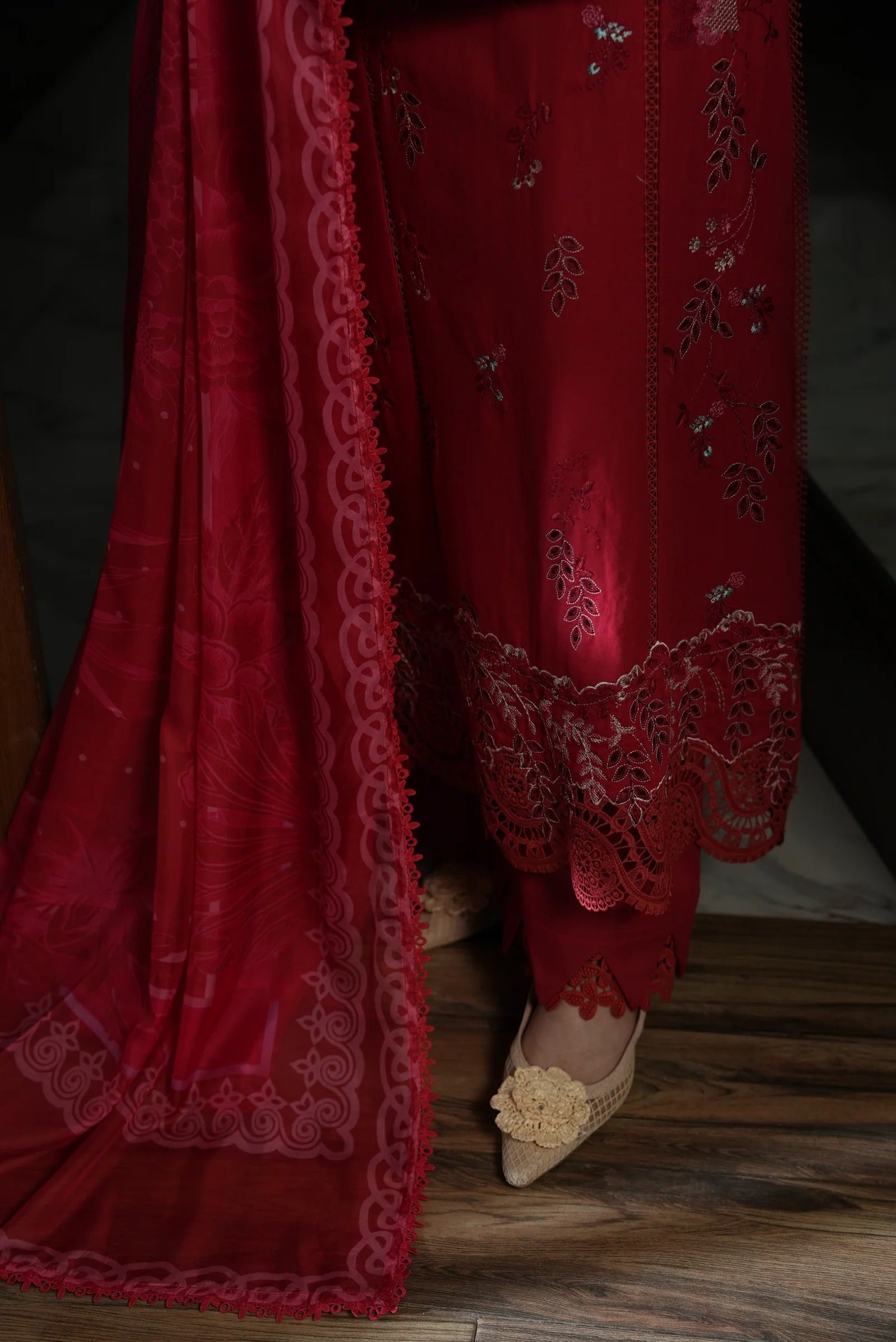 Red embroidered fabric with a close-up of intricate patterns on a wooden floor.