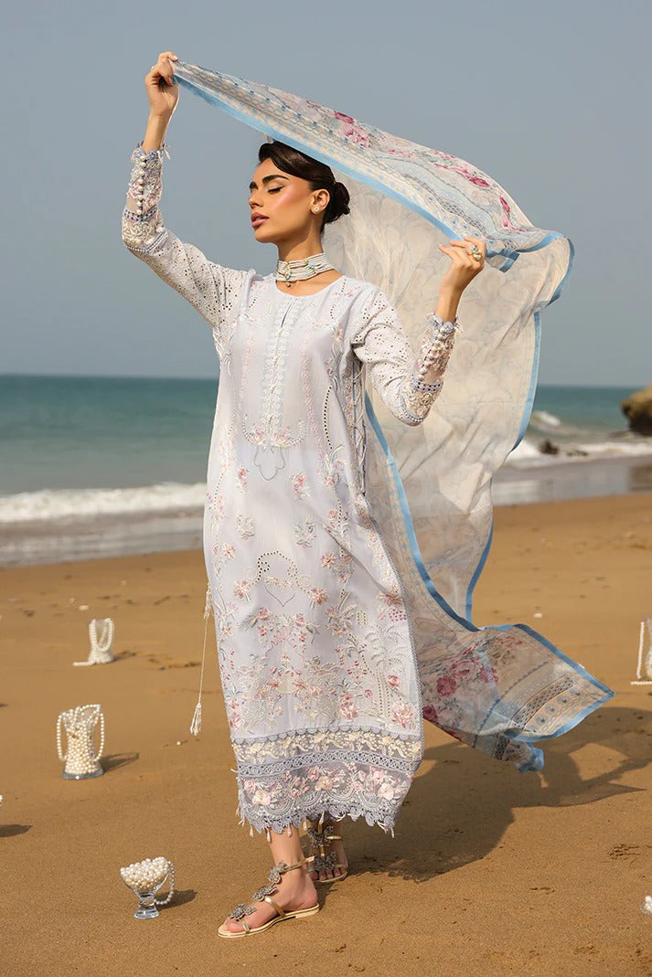 Woman in a light blue embroidered outfit on a beach with ocean in the background