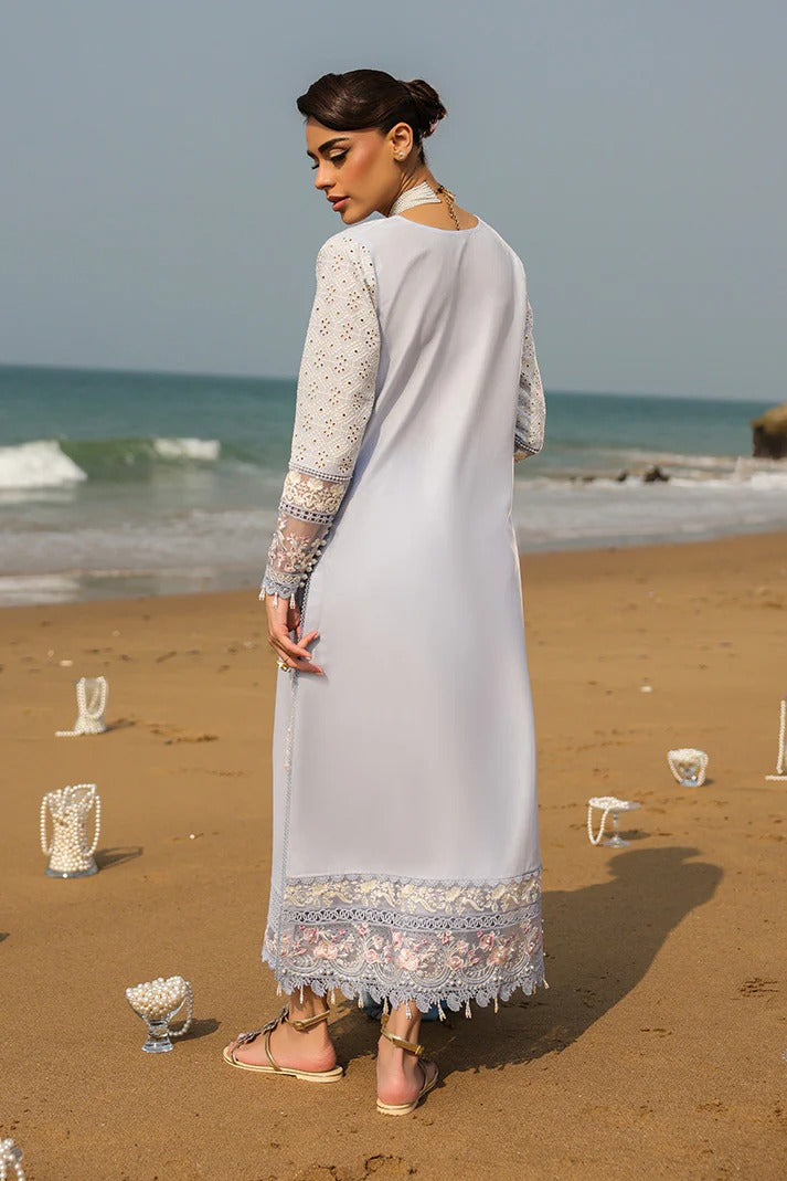 Woman in a long, light-colored dress standing on a beach with ocean waves in the background.