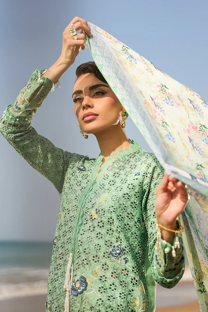Woman in a green traditional outfit with a floral scarf, standing by the beach.