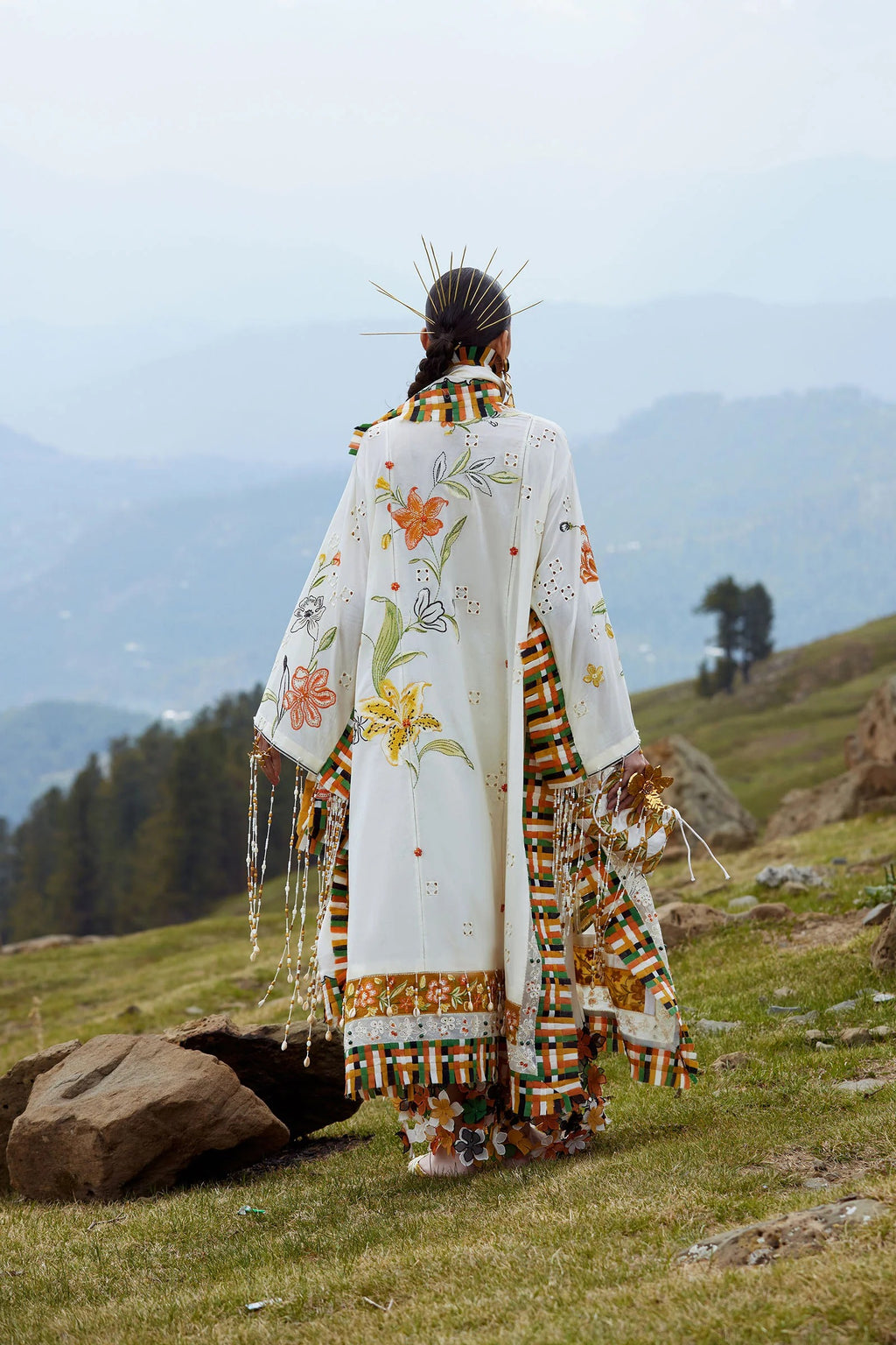 Person wearing a traditional outfit with floral patterns in a mountainous landscape